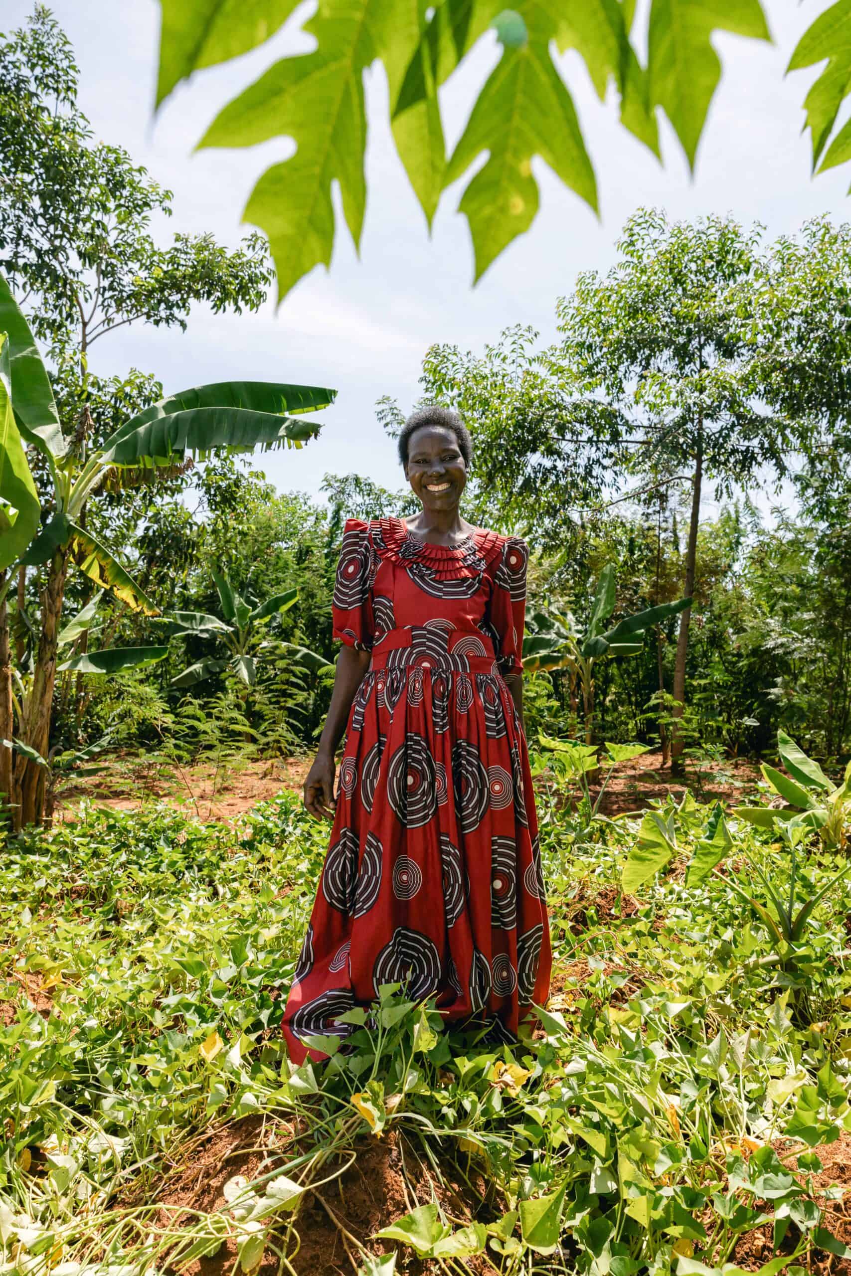 Smiling woman in vibrant dress standing amidst lush green plants supported by Trees for the Future