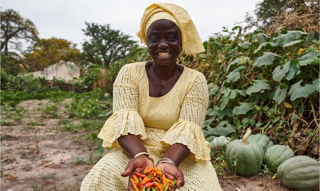 A smiling woman, part of TREES ambassadors, in a garden holding freshly harvested peppers.